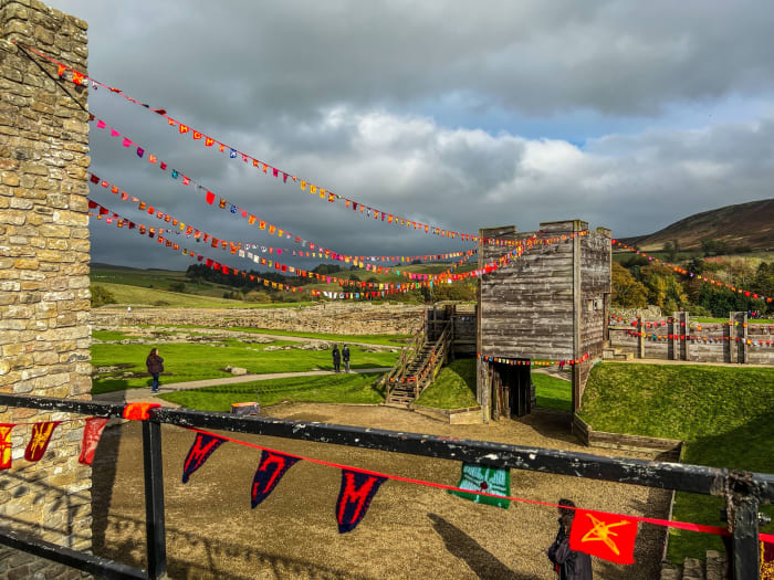 Multicoloured flags of Bunting strung between two towers with Vindolanda fort stretching out behind.